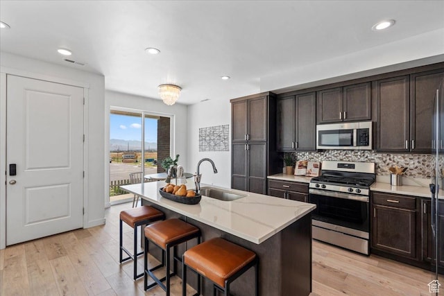 11568 S Watercourse Rd, South Jordan, UT 84009 - kitchen featuring appliances with stainless steel finishes, tasteful backsplash, dark brown cabinetry, a breakfast bar area, and light wood-type flooring