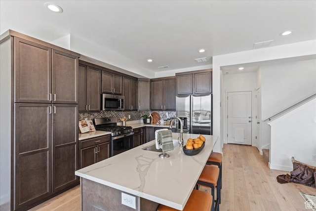 11568 S Watercourse Rd, South Jordan, UT 84009 - kitchen featuring stainless steel appliances, dark brown cabinets, a kitchen breakfast bar, light wood-type flooring, and backsplash