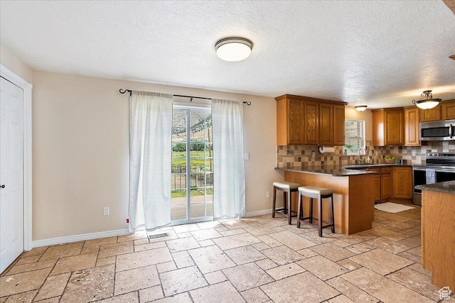 315 E 900 N, Brigham City, UT 84302 - kitchen with stainless steel appliances, decorative backsplash, a peninsula, brown cabinets, and stone tile floors