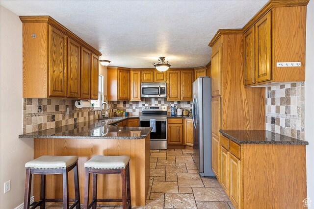 315 E 900 N, Brigham City, UT 84302 - kitchen featuring appliances with stainless steel finishes, a peninsula, brown cabinetry, stone tile flooring, and backsplash