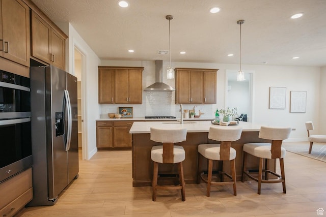 3 Rosalia Rdg, St George, UT 84770 - kitchen featuring appliances with stainless steel finishes, wall chimney exhaust hood, brown cabinetry, light wood-type flooring, and recessed lighting