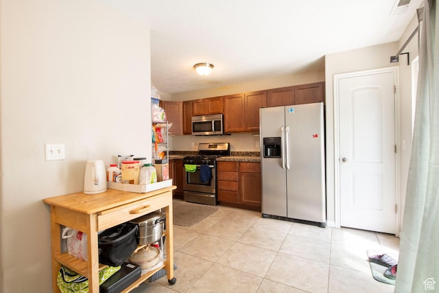 3408 S Carrick Dr W, South Salt Lake, UT 84115 - kitchen with stainless steel appliances, brown cabinetry, light tile patterned floors, and dark countertops