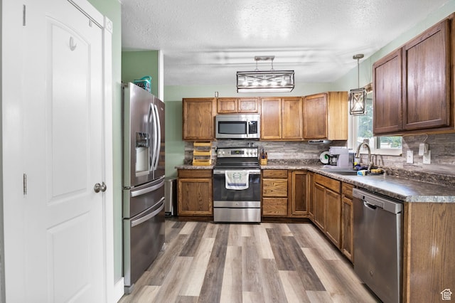 4895 W Pavant Ave, West Valley City, UT 84120 - kitchen with stainless steel appliances, light wood-style floors, a textured ceiling, dark countertops, and brown cabinets