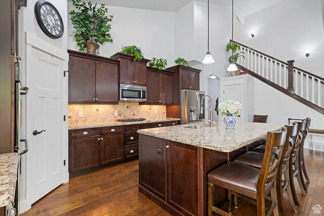 6923 W Long Ridge Dr S, Herriman, UT 84096 - kitchen featuring appliances with stainless steel finishes, dark wood-style flooring, decorative backsplash, a breakfast bar area, and a kitchen island with sink