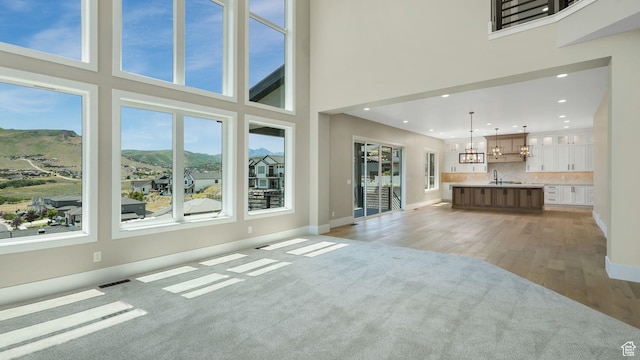 7233 W Summit Top Ln, Herriman, UT 84096 - unfurnished living room featuring a mountain view, a chandelier, light wood finished floors, a high ceiling, and recessed lighting