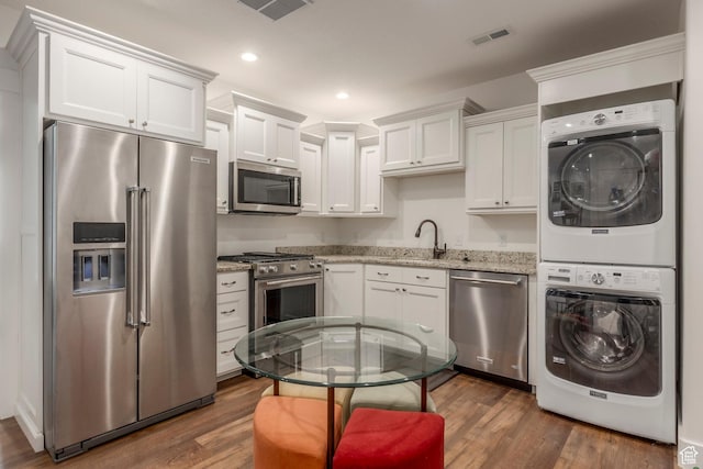 9532 S Willow Trail Way S, Jordan, UT 84095 - kitchen featuring appliances with stainless steel finishes, stacked washer / dryer, light stone countertops, white cabinetry, and dark wood-style flooring