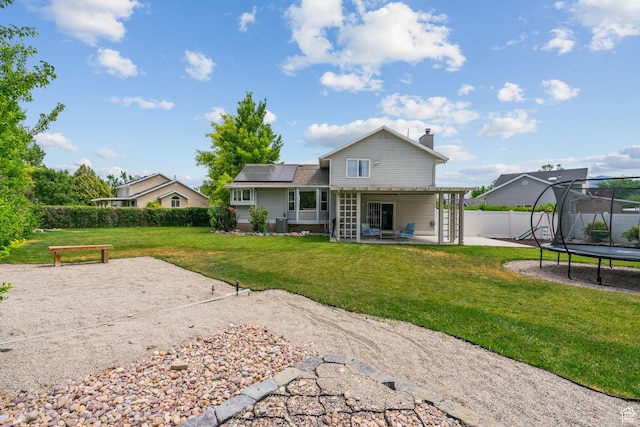 13082 S 2770th Cir W, Riverton, UT 84065 - back of house featuring a trampoline, a patio, roof mounted solar panels, a chimney, and a fenced backyard