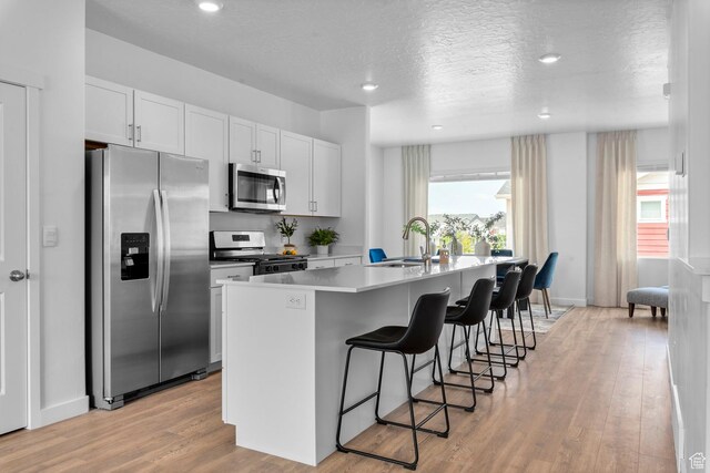 1288 N 375 E Unit 147, Harrisville, UT 84404 - kitchen featuring stainless steel appliances, a kitchen breakfast bar, a center island with sink, light wood-type flooring, and white cabinets
