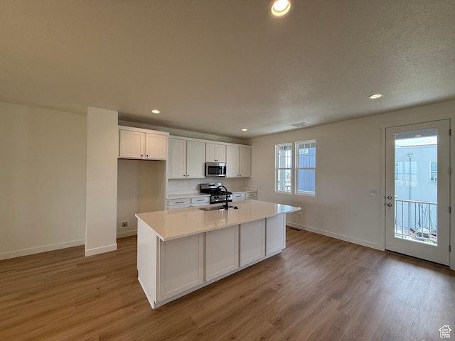 6921 W S Jordan Pkwy Unit 310, South Jordan, UT 84009 - kitchen featuring stainless steel appliances, light wood-style floors, white cabinetry, light countertops, and a kitchen island with sink