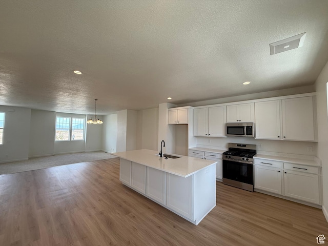 6921 W S Jordan Pkwy Unit 310, South Jordan, UT 84009 - kitchen with stainless steel appliances, a textured ceiling, a chandelier, light wood-style floors, and white cabinetry