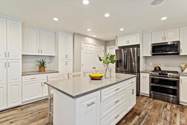 53 N Foxhill Rd N, North Salt Lake, UT 84054 - kitchen with appliances with stainless steel finishes, wood finished floors, white cabinets, a kitchen breakfast bar, and recessed lighting