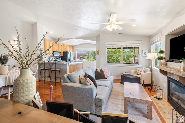 1692 E Kelmscott Ct S Unit C, Salt Lake City, UT 84124 - living room featuring vaulted ceiling, a tiled fireplace, a ceiling fan, light wood-style floors, and a textured ceiling