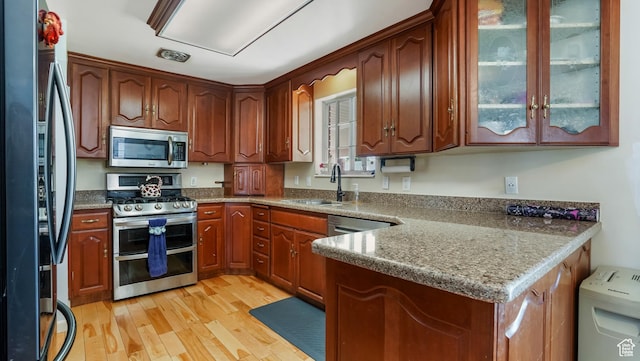 176 E Brook Ave N, Tooele, UT 84074 - kitchen featuring stainless steel appliances, light wood finished floors, glass insert cabinets, a peninsula, and dark stone countertops