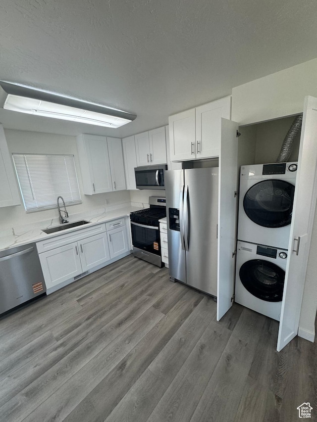 3923 W 5820 S, Taylorsville, UT 84118 - kitchen with appliances with stainless steel finishes, stacked washer and clothes dryer, white cabinetry, wood finished floors, and light countertops