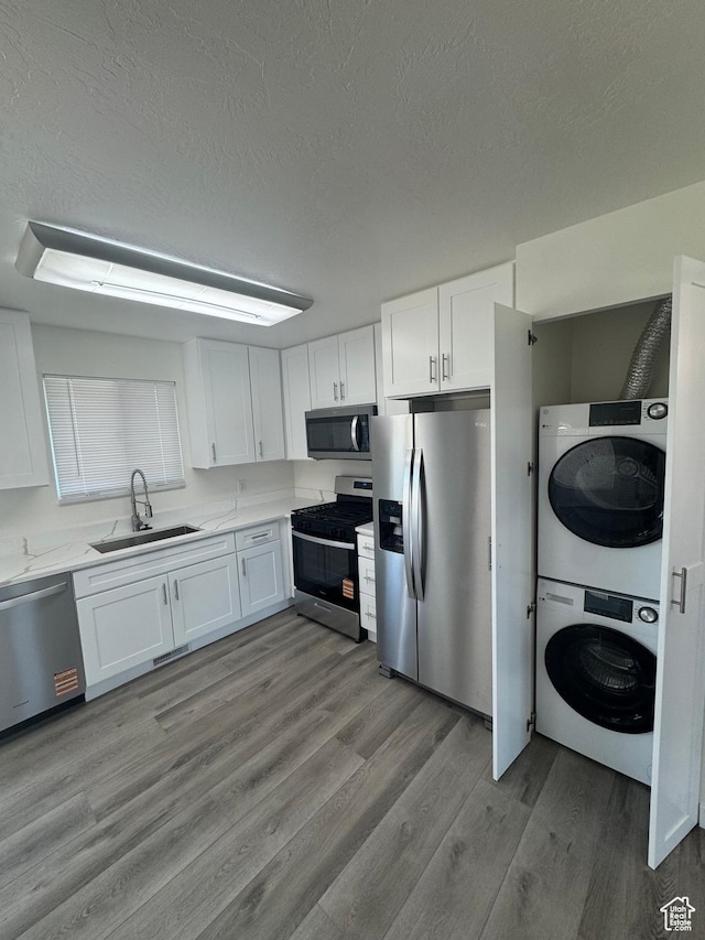 3923 W 5820 S, Taylorsville, UT 84118 - kitchen with appliances with stainless steel finishes, stacked washer and clothes dryer, white cabinets, wood finished floors, and a textured ceiling
