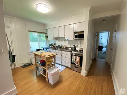 1309 E Hidden Creek Ct S, Holladay, UT 84117 - kitchen featuring stainless steel appliances, light wood finished floors, dark countertops, white cabinets, and crown molding