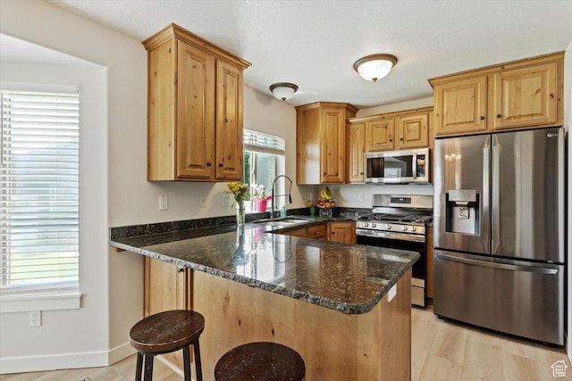 2876 S 1200 W, Syracuse, UT 84075 - kitchen with stainless steel appliances, dark stone counters, a peninsula, a kitchen breakfast bar, and light wood finished floors