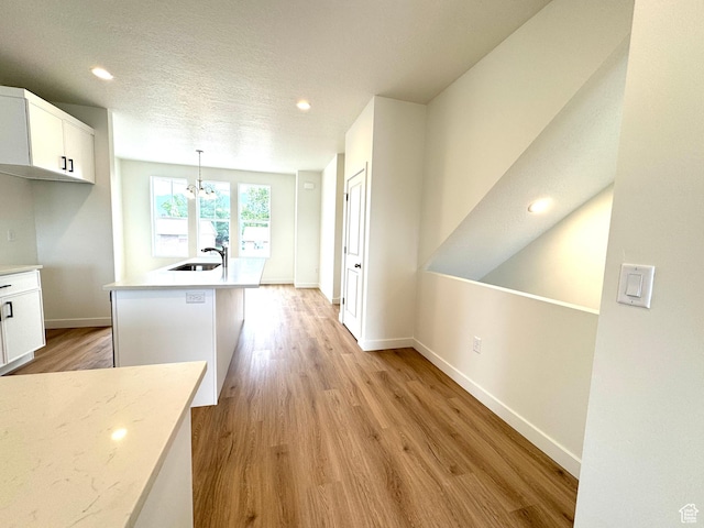 1650 N Main St N Unit 116, Layton, UT 84041 - kitchen featuring a chandelier, white cabinets, light wood-type flooring, hanging light fixtures, and a kitchen island with sink