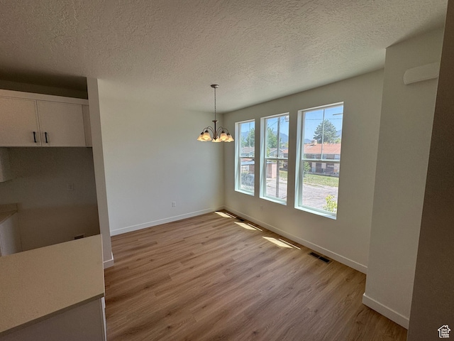1650 N Main St N Unit 116, Layton, UT 84041 - unfurnished dining area with light wood-type flooring, a chandelier, and a textured ceiling