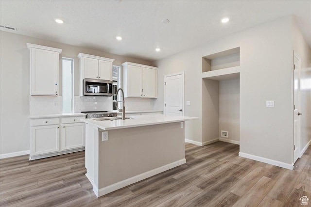 6168 W Franciscotti Dr Unit 605, South Jordan, UT 84009 - kitchen with stainless steel microwave, light wood finished floors, a kitchen island with sink, tasteful backsplash, and recessed lighting