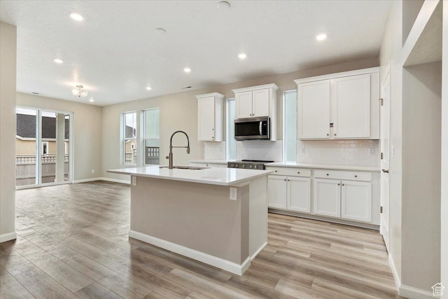 6168 W Franciscotti Dr Unit 605, South Jordan, UT 84009 - kitchen with stainless steel microwave, light wood-style floors, a kitchen island with sink, tasteful backsplash, and recessed lighting