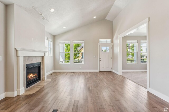 11103 S Kiwano Way W, South Jordan, UT 84009 - unfurnished living room with a tile fireplace, wood finished floors, healthy amount of natural light, vaulted ceiling, and a textured ceiling