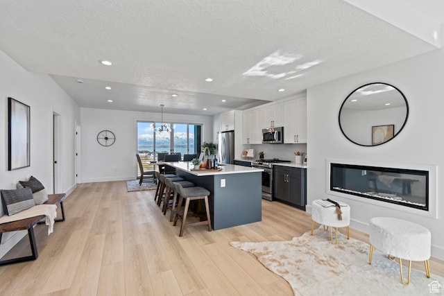 79 E Watson Dr, Saratoga Springs, UT 84045 - kitchen with appliances with stainless steel finishes, a center island, a breakfast bar area, light wood finished floors, and a textured ceiling