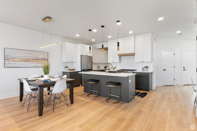 78 Watson Dr, Saratoga Springs, UT 84045 - kitchen with stainless steel refrigerator, light wood-style flooring, light countertops, a kitchen island with sink, and backsplash