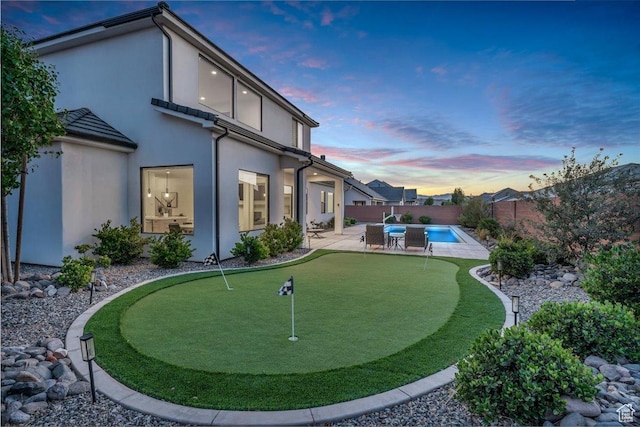 529 E 4290 S, Washington, UT 84780 - back of house at dusk featuring a putting green, a patio, a fenced backyard, and stucco siding