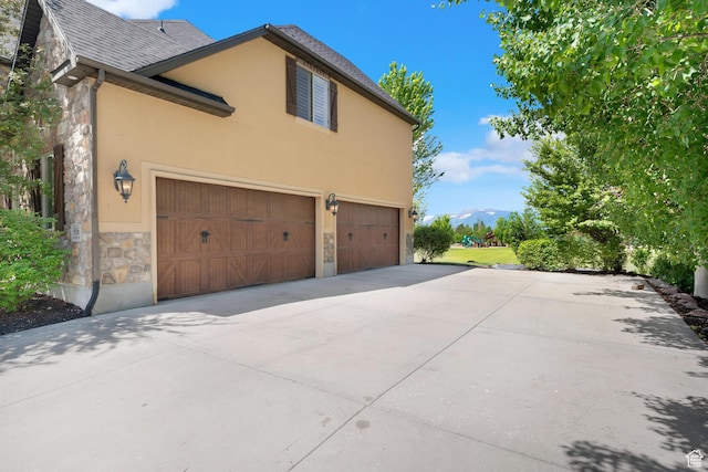 916 Ledgestone Ln, Heber City, UT 84032 - view of side of home with stone siding, an attached garage, driveway, stucco siding, and a shingled roof