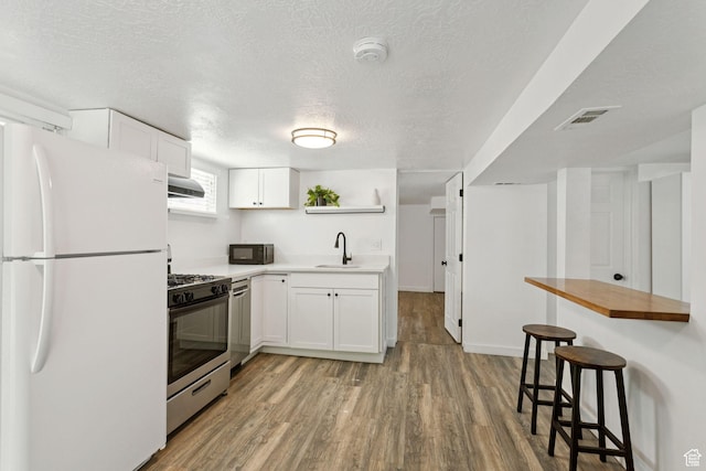 1163 E Blaine Ave, Salt Lake City, UT 84105 - kitchen with stainless steel appliances, light wood-style flooring, a kitchen bar, white cabinetry, and a textured ceiling