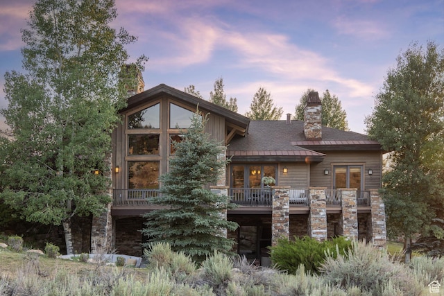 2711 E Bitter Brush Dr, Park City, UT 84098 - back of house at dusk featuring stone siding, a chimney, and a balcony