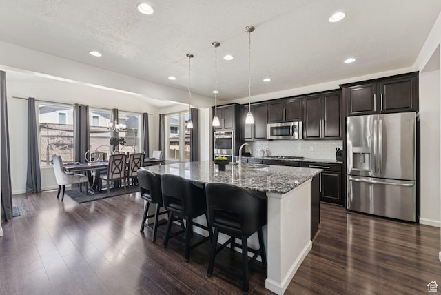5488 W Tower Arch Ln, Herriman, UT 84096 - kitchen with appliances with stainless steel finishes, a center island with sink, dark wood finished floors, a breakfast bar area, and recessed lighting