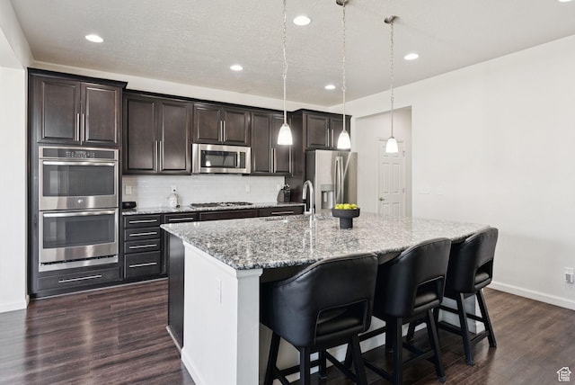 5488 W Tower Arch Ln, Herriman, UT 84096 - kitchen featuring stainless steel appliances, an island with sink, dark wood-style floors, dark brown cabinetry, and tasteful backsplash