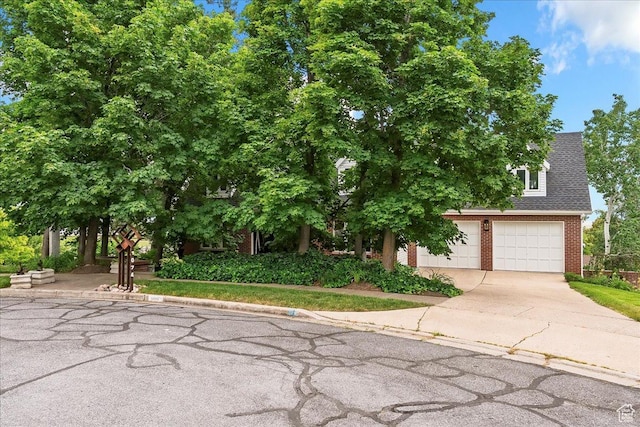 1074 E Raymond Rd, Fruit Heights, UT 84037 - view of property hidden behind natural elements with brick siding, concrete driveway, a garage, and a shingled roof