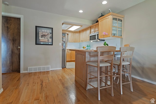 8216 S Scandia Way, Sandy, UT 84093 - kitchen with appliances with stainless steel finishes, light brown cabinetry, light wood-style floors, a breakfast bar area, and glass insert cabinets
