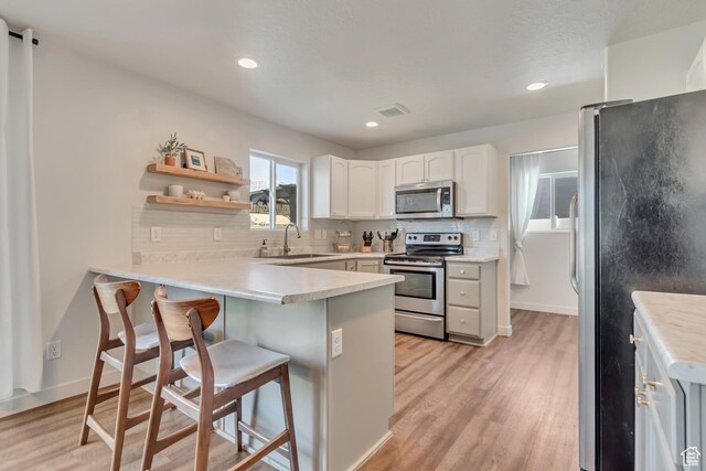 442 N Cowan Cir E, Payson, UT 84651 - kitchen with stainless steel appliances, a peninsula, backsplash, a breakfast bar area, and light wood-type flooring