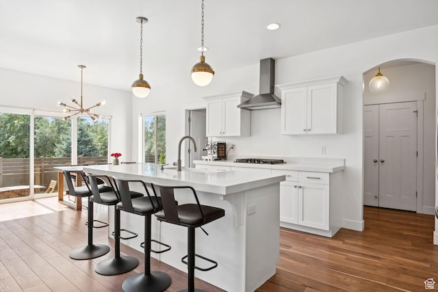 67 N 300 E, Vineyard, UT 84059 - kitchen featuring wall chimney exhaust hood, cooktop, arched walkways, light countertops, and an island with sink