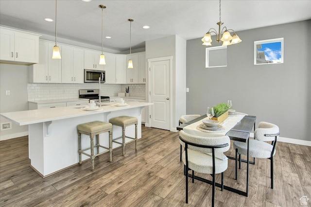 12232 S Sigmon Ln, Herriman, UT 84096 - kitchen featuring stainless steel appliances, an island with sink, decorative backsplash, white cabinets, and wood finished floors