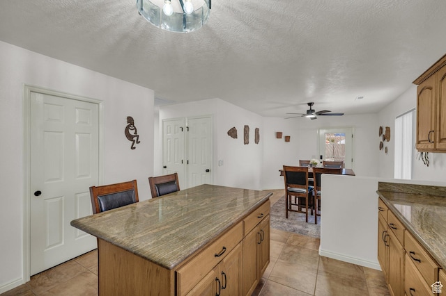 504 E Telegraph St Unit 89, Washington, UT 84780 - kitchen with a kitchen island, ceiling fan, light tile patterned floors, dark stone countertops, and a textured ceiling