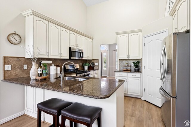 1036 E Fairway Dr, North Salt Lake, UT 84054 - kitchen featuring appliances with stainless steel finishes, a peninsula, light wood-style floors, backsplash, and dark stone counters