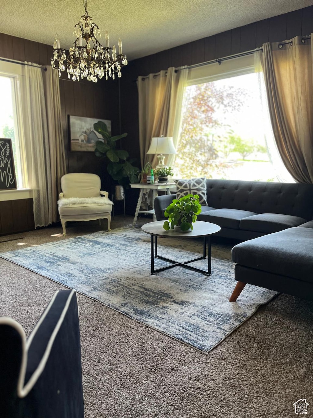 148 E Center St, Clarkston, UT 84305 - living room featuring carpet floors, a chandelier, a textured ceiling, and wooden walls