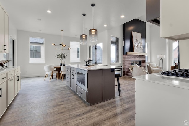 4269 N Maple Hollow Dr Unit 117, Lehi, UT 84043 - kitchen featuring a brick fireplace, light wood-style flooring, gas stovetop, stainless steel microwave, and a breakfast bar area