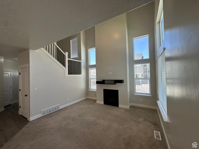 1738 W Terra Vis, Saratoga Springs, UT 84045 - unfurnished living room with a high ceiling, carpet floors, a fireplace, a textured ceiling, and stairway