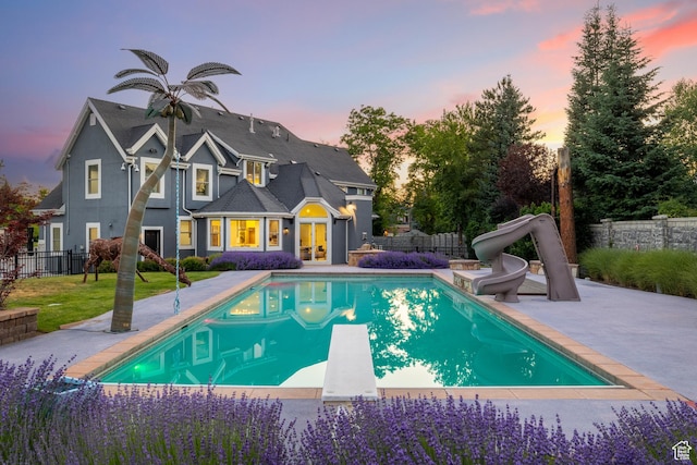6273 S Oakcrest Cir, Holladay, UT 84121 - pool at dusk with a water slide, a patio, a diving board, and a fenced backyard