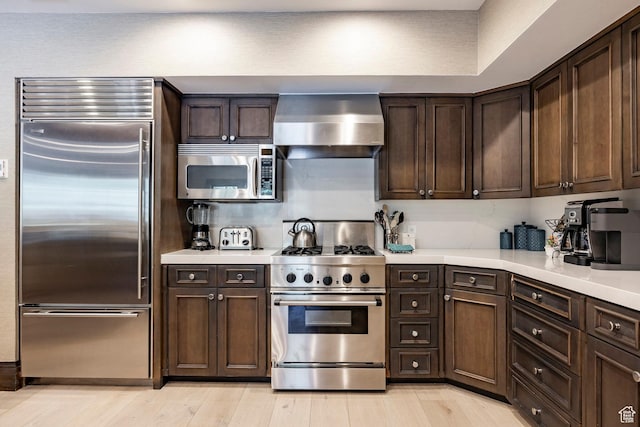 7815 Royal St Unit C259, Park City, UT 84060 - kitchen featuring high quality appliances, wall chimney exhaust hood, dark brown cabinetry, light countertops, and light wood finished floors