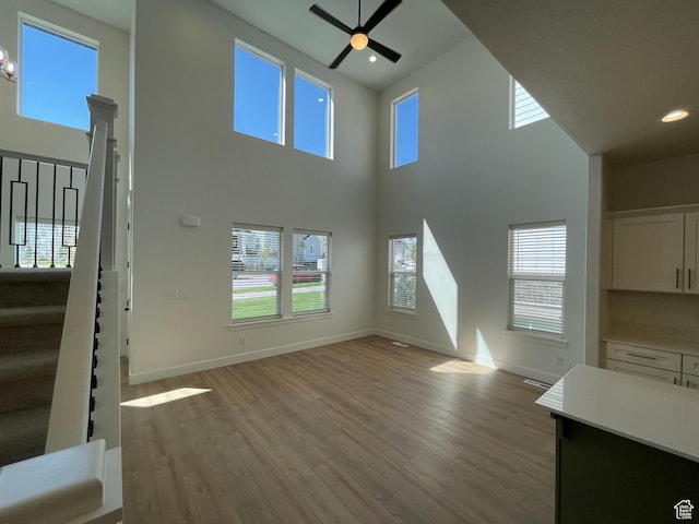4332 W Watchmen Way, Herriman, UT 84096 - unfurnished living room featuring stairway, light wood finished floors, a ceiling fan, plenty of natural light, and a high ceiling
