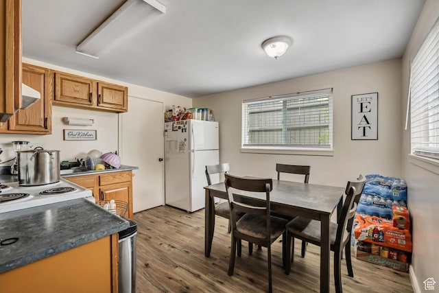 222 W Center St S, Midvale, UT 84047 - kitchen with freestanding refrigerator, wood finished floors, brown cabinetry, dark countertops, and ventilation hood