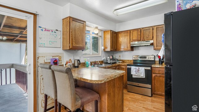 636 Downs Dr, Ogden, UT 84404 - kitchen with freestanding refrigerator, stainless steel electric range oven, under cabinet range hood, a peninsula, and brown cabinetry