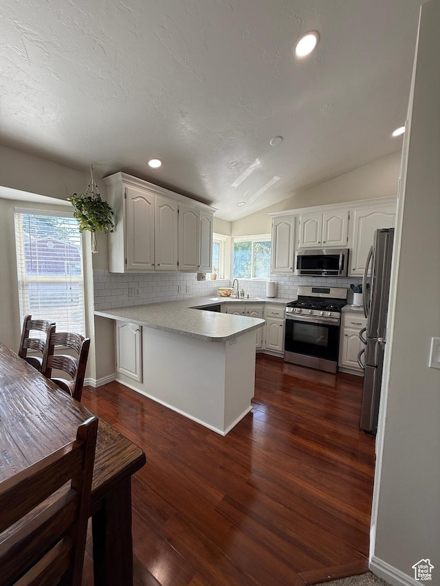 14048 S Van Cott Peak Cir W, Riverton, UT 84096 - kitchen with appliances with stainless steel finishes, decorative backsplash, a peninsula, white cabinets, and vaulted ceiling